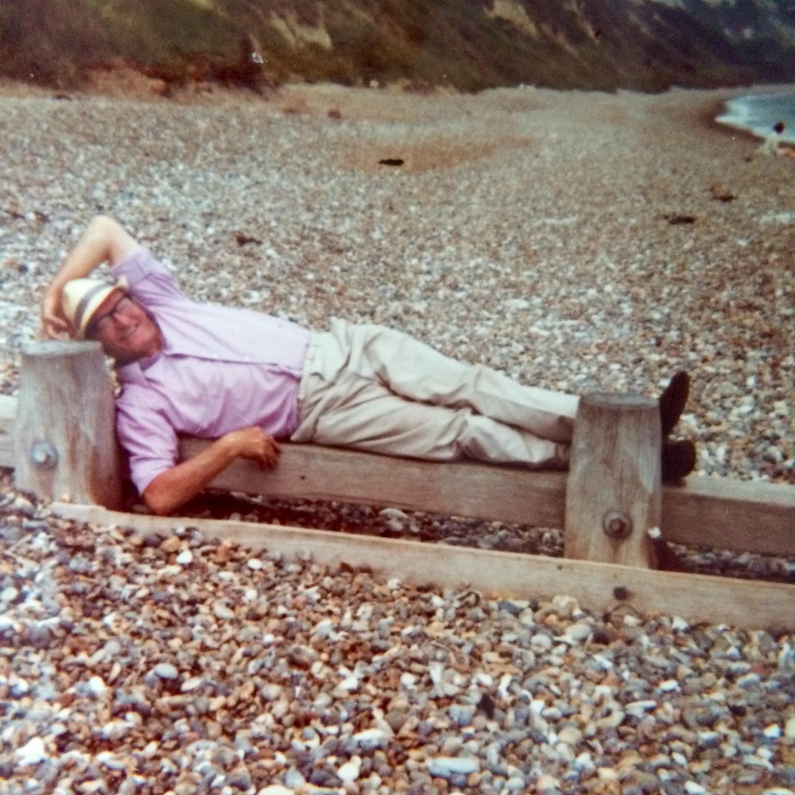 Stan Edwards reclining on a wooden groyne on a pebble beach